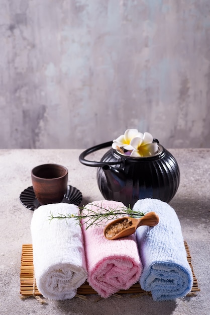 Asciugamani di colore con foglie verdi, cucchiaio di sale e tè di disintossicazione sul tappetino di bambù e tavolo in pietra