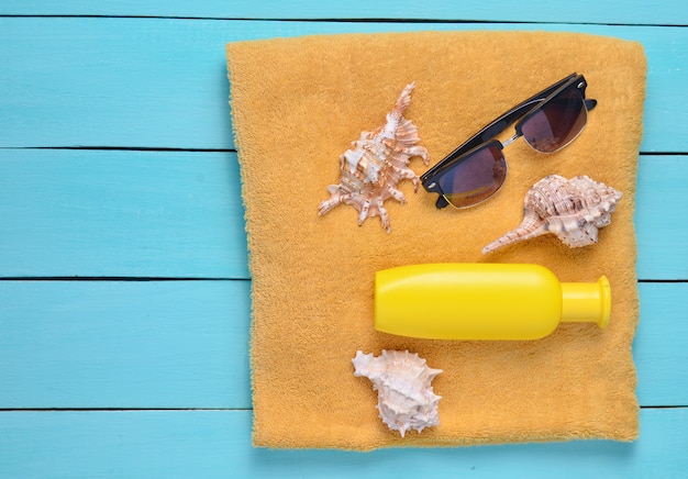 Asciugamano con crema solare, cockleshells, occhiali da sole su assi di legno blu