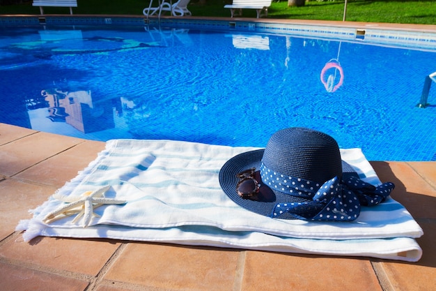 Asciugamano e cappello estivo vicino alla piscina durante la soleggiata giornata estiva