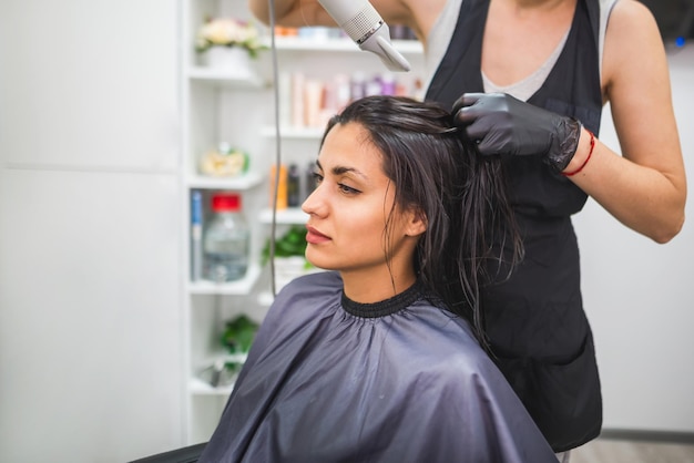 Asciugare i capelli lunghi e scuri con un asciugacapelliparrucchiere professionista asciuga i capelli di un cliente nel salone acconciatura bellezza cura dei capelli servizio di moda