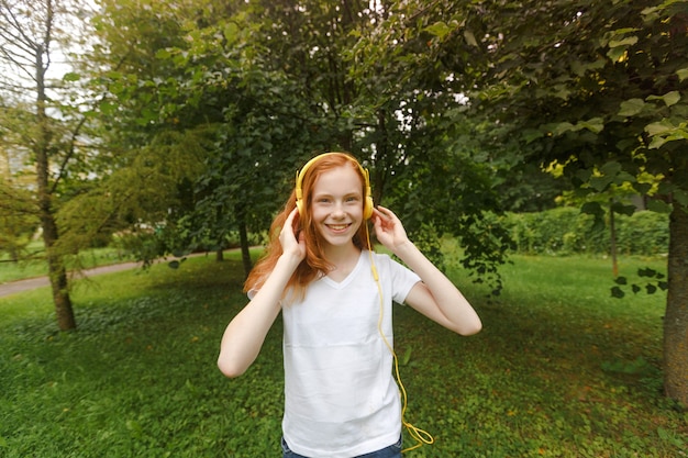 Ascolta la musica mentre ti rilassi all'aria aperta. Il bambino gode della musica dell'erba verde del prato. Tempo piacevole Bella ragazza con i capelli rossi in cuffia che ascolta la musica.