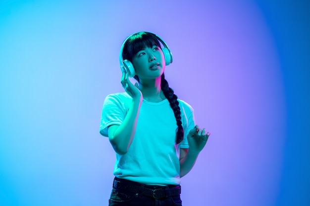 Ascoltare musica, ballare in cuffia. Ritratto di giovane donna asiatica su studio sfumato blu-viola