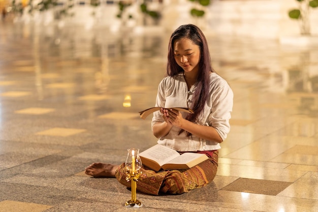 Asia donna che indossa abiti tradizionali della Thailandia leggendo il sanscrito antico libro Tripitaka e il libro del Dharma del Signore Buddha dhamma nella notte lanterna a candela