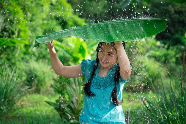 Asia donna con i capelli neri che tiene una foglia di banana sotto la pioggia