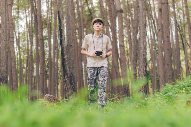 Asia uomo indossa camicia, cappello e pantaloni mimetici, cammina e scatta foto nella foresta