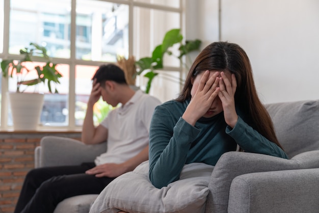 Asian couple have problems beign in quarrel sitting on sofa in living room and young woman is very upset and crying