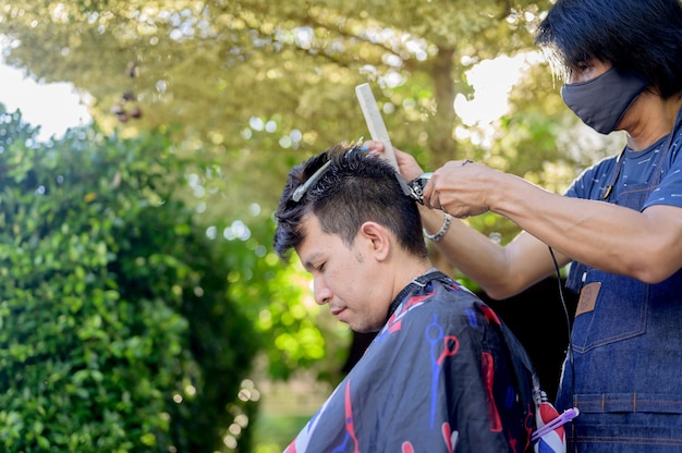 Asian facendo taglio di capelli nel giardino di casa. Imparare i corsi di barbiere online durante il blocco per una nuova occupazione. Nuova vita normale dopo la situazione pandemica dell'epidemia di Covid-19.