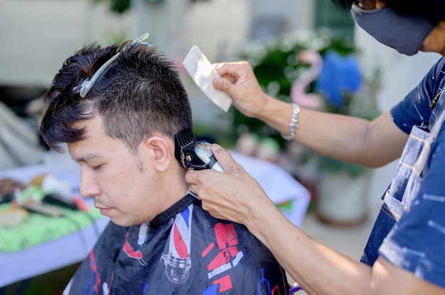 Asian facendo taglio di capelli nel giardino di casa. Imparare i corsi di barbiere online durante il blocco per una nuova occupazione. Nuova vita normale dopo la situazione pandemica dell'epidemia di Covid-19.