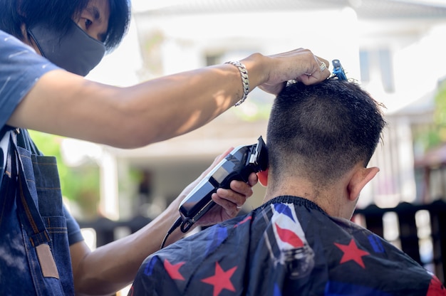 Asian facendo taglio di capelli nel giardino di casa. Imparare i corsi di barbiere online durante il blocco per una nuova occupazione. Nuova vita normale dopo la situazione pandemica dell'epidemia di Covid-19.