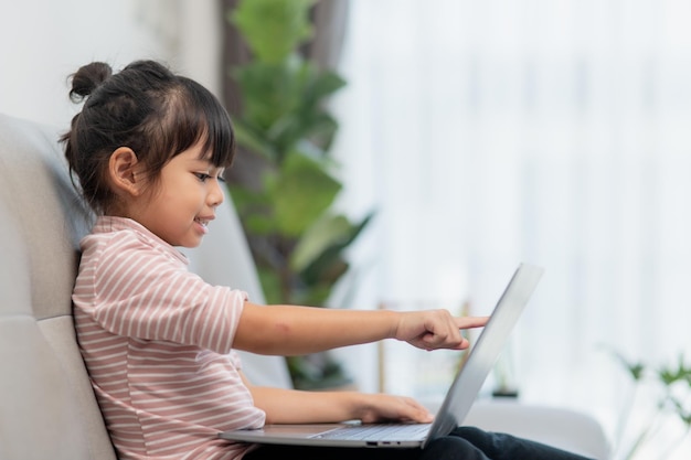 Asian Little school kid girl usa il computer portatile seduto sul divano da solo a casa