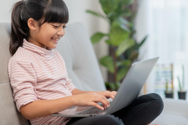 Asian Little school kid girl usa il computer portatile seduto sul divano da solo a casa