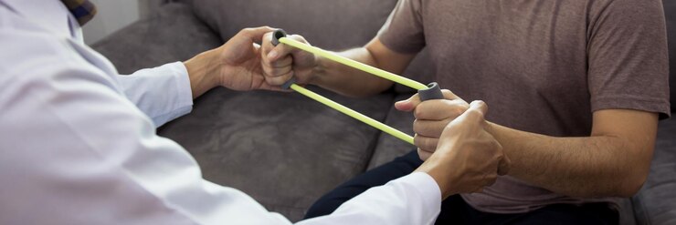 Asian male physical therapist descent working and helping to protect the hands of patients with patient doing stretching exercise with a flexible exercise band in clinic room