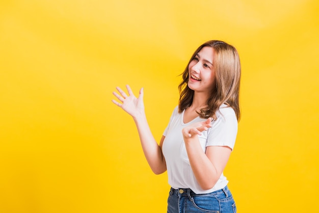 Asian Thai felice ritratto bella giovane donna carina in piedi indossare t-shirt la sua vincente e sorpresa eccitata urla bocca aperta mostrando le mani, girato in studio isolato sfondo giallo con spazio di copia