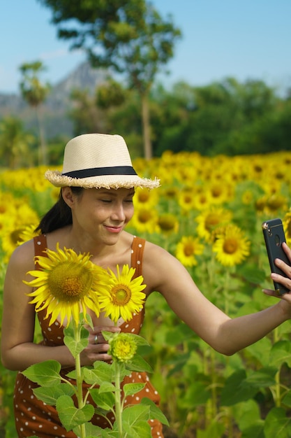 Asian Woman 40s LGBT transgender express feeling Happy Smile mobile selfie sotto il sole Campo di fiori gialli girasole sopra la montagna del cielo blu La femmina posa per le riprese di moda nel paesaggio all'aperto