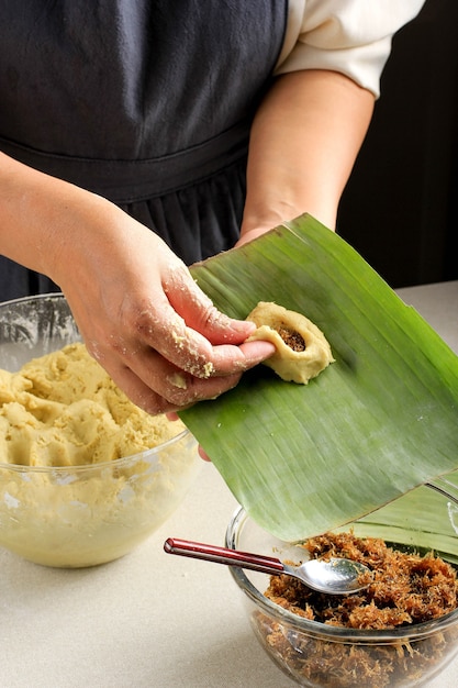 Asian Woman Hand Making Bugis, cibo tradizionale a base di farina di riso glutinoso riempito con una miscela di zucchero e cocco grattugiato (Unti), quindi avvolto in foglie di banana e al vapore, sapore dolce.