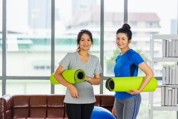 Asiatica adulta e giovane donna sorridente che tiene un tappetino da yoga dopo lo yoga e l'esercizio Ritratto di una donna felice e bella in piedi che tiene il tappetino da yoga in studio indoor sport concetto di allenamento sano