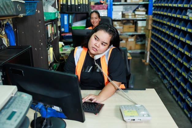 Asiatica bella donna grassa magazziniere che parla per telefono ordine del cliente nel computer desktop presso la fabbrica del magazzino dell'ufficio Plus size donne che ispezionano i prodotti che lavorano