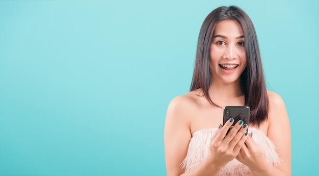 Asiatica ritratto felice bella giovane donna in piedi sorriso lei tenendo smartphone o telefono cellulare e cercando di fotocamera su sfondo blu con copia spazio per il testo