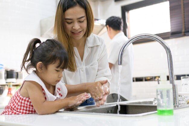 Asiatico della figlia e della madre che si lava le sue mani con sapone nel lavandino di una cucina