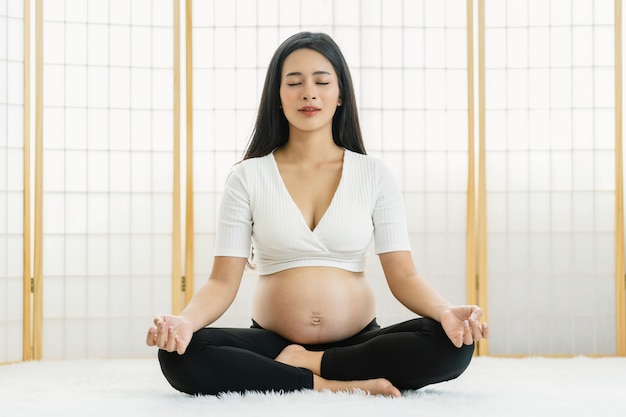 Asiatico incinto facendo esercizi con yoga sedendosi e meditando in casa in stile giapponese