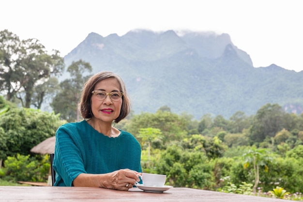 Asin donna senior che beve caffè nella caffetteria all'aperto con vista sulle montagne