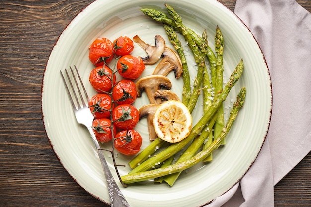 Asparagi al forno con pomodorini e limone in un piatto su una superficie di legno. Lay piatto