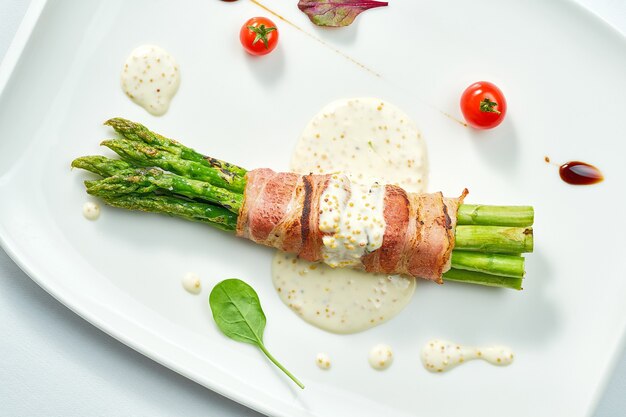 Asparagi alla griglia con pancetta e salsa di senape in un piatto bianco. Isolato su superficie bianca.