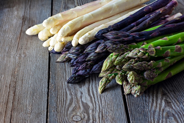 Asparagi bianchi, viola, verdi grezzi su un fondo di legno scuro. Concetto di cibo crudo, posto per copia spazio.