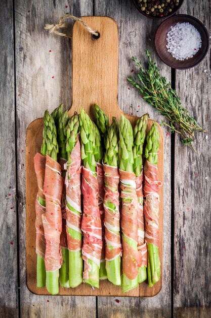 Asparagi biologici freschi avvolti nel prosciutto di Parma su un tagliere vista dall'alto