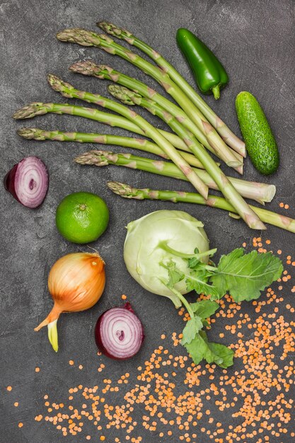 Asparagi, cetrioli, lime e cavolo rapa, cipolle e lenticchie rosse sul tavolo. Sfondo nero. Disposizione piatta.