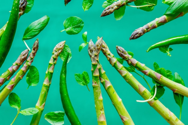 Asparagi freschi e foglie di basilico sulla superficie verde.