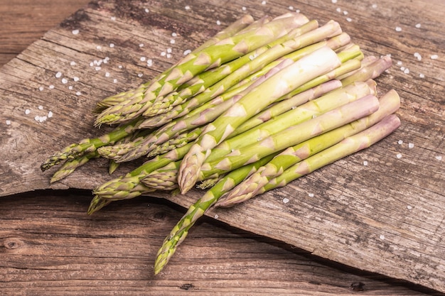 Asparagi maturi pronti per la cottura. Supporti in legno vintage, luce intensa, ombra scura. Sfondo di vecchie schede, spazio di copia