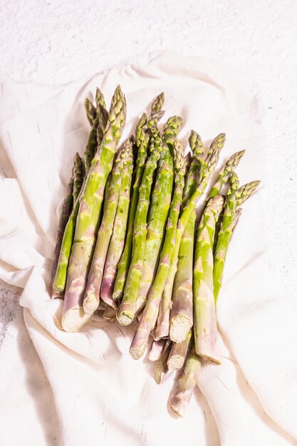 Asparagi maturi su un tovagliolo di lino vintage. Ingredienti verdi freschi pronti per cucinare cibi sani. Luce dura moderna, ombra scura. Sfondo in gesso bianco, copia spazio