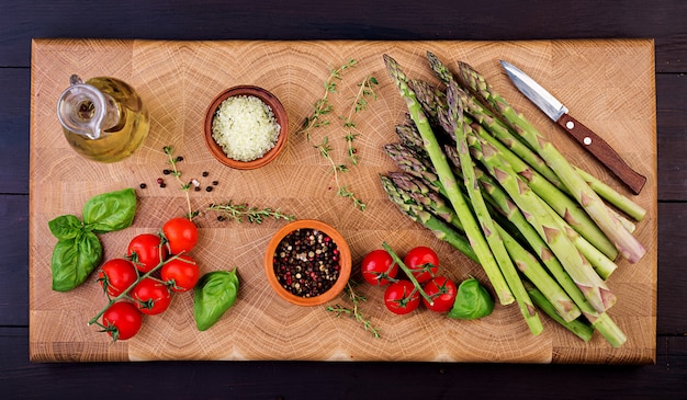 Asparagi verdi freschi con i pomodori e le erbe su una tavola di legno rustica