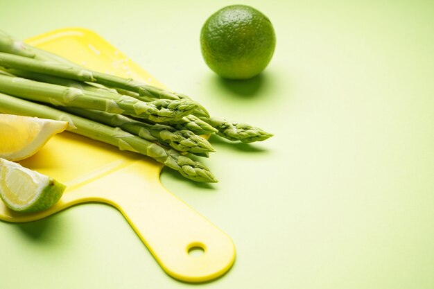 Asparagi verdi su tavola da cucina con limone e lime su superficie verde, posto per il testo