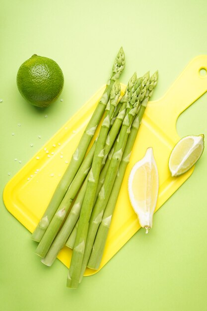 Asparagi verdi su tavola da cucina con limone e lime sulla superficie verde. Avvicinamento