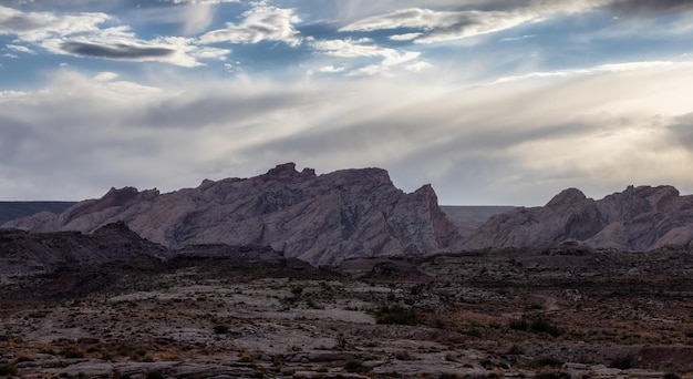 Aspre formazioni rocciose di montagna nel deserto con nuvole drammatiche al tramonto