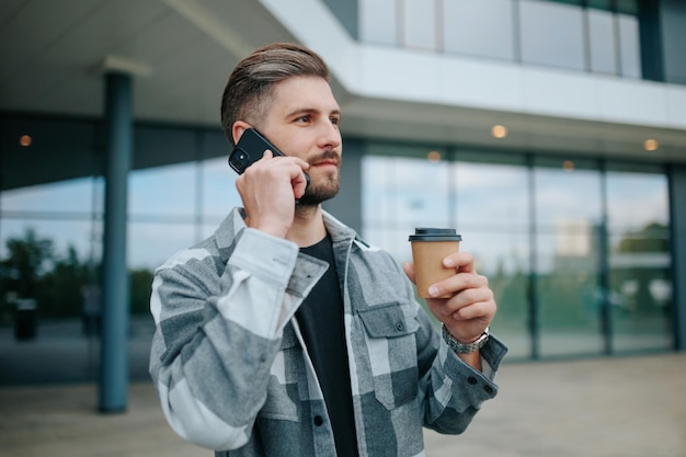 Assaporando la città un ragazzo simpatico con una tazza chiacchiera al cellulare nelle conversazioni cittadine all'aria aperta