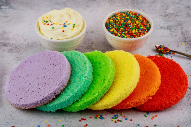 Assemblare la torta a strati arcobaleno con crema bianca e codette.