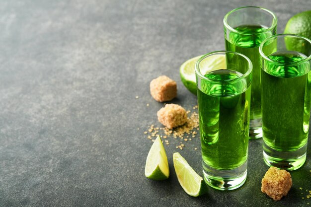 Assenzio Due bicchieri di assenzio con zucchero di canna e lime su sfondo scuro Bevanda alcolica forte Concetto di carta Bar Posto per il testo