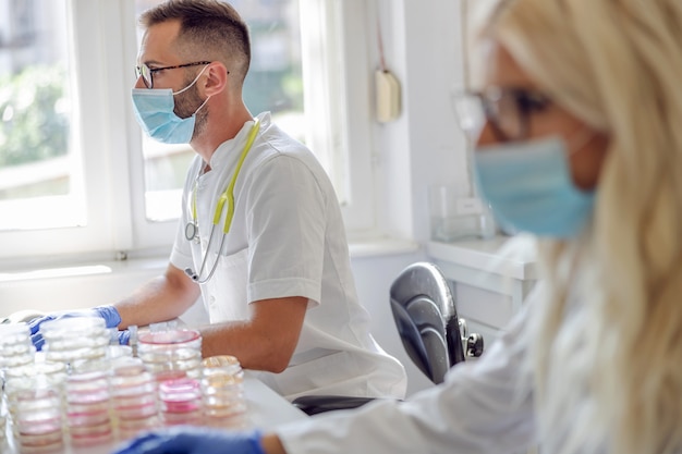 Assistente di laboratorio attraente maschio seduto in laboratorio e lavorando alla ricerca per il vaccino contro il virus corona.