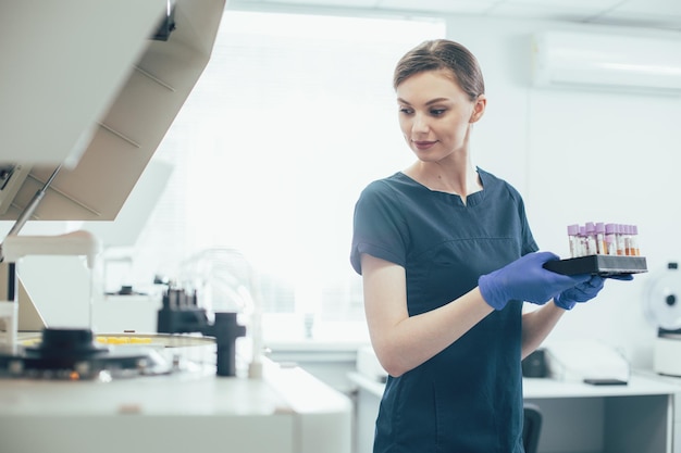 Assistente di laboratorio calmo che trasporta le provette in un supporto e si gira verso la macchina per centrifuga