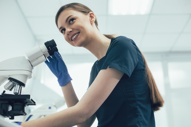 Assistente di laboratorio positivo che indossa guanti di gomma sterili mentre si tocca un microscopio