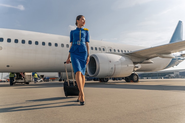 Assistente di volo femminile che cammina con la valigia nera