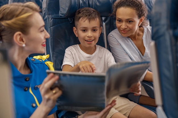 Assistente di volo femminile che intrattiene un bambino a bordo offrendo un libro da leggere. L'equipaggio di cabina fornisce un servizio alla famiglia in aereo. Trasporto aereo e concetto di turismo