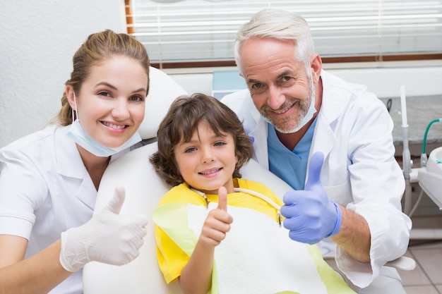 Assistente e ragazzino pediatrici del dentista che sorridono alla macchina fotografica con i pollici su