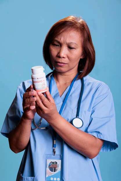 Assistente medico serio che lavora al trattamento farmacologico per prevenire la malattia del paziente, tenendo la scatola dei farmaci leggendo il foglietto illustrativo farmaceutico in studio con sfondo blu. Servizio e concetto di assistenza sanitaria