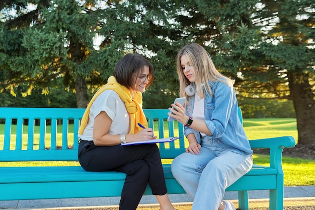 Assistente sociale femminile, psicologa, giornalista, registrando intervistando una studentessa adolescente. Donne sedute su una panchina nel parco