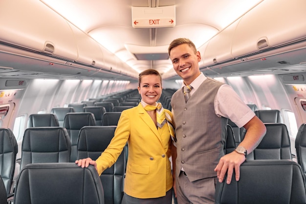 Assistenti di volo gioiosi di uomini e donne che guardano la fotocamera e sorridono mentre mettono le mani sui sedili dei passeggeri