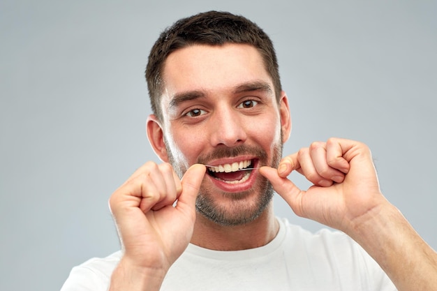 assistenza sanitaria, igiene dentale, persone e concetto di bellezza - giovane sorridente con il filo interdentale che pulisce i denti su sfondo grigio